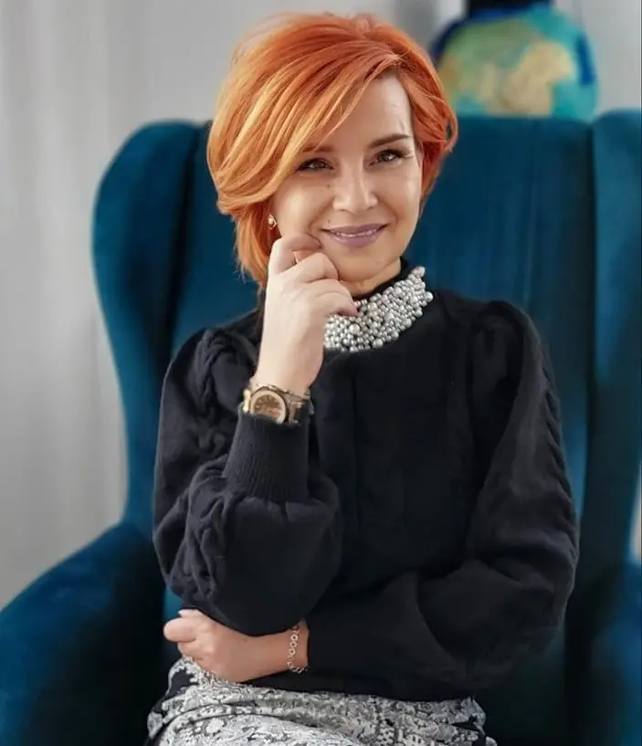 Psihoterapeut Carmen Gavrilescu într-o postură profesională, zâmbitoare, într-un fotoliu elegant – psiholog specializat în constelații familiale și dezvoltare personală